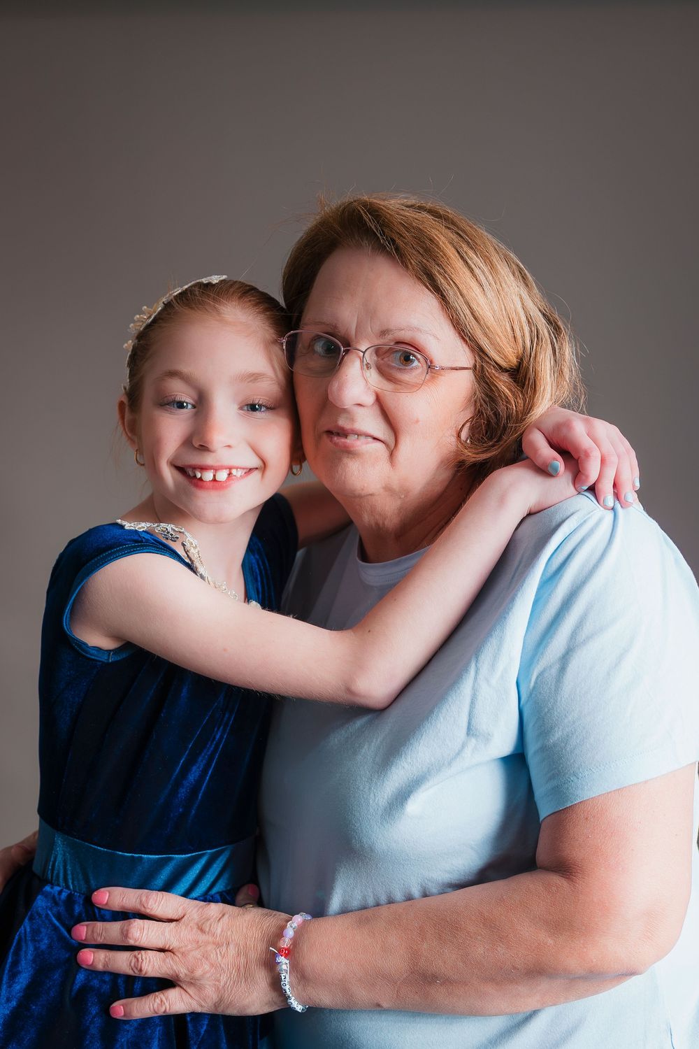An affectionate portrait of two generations embracing against a neutral gray background.