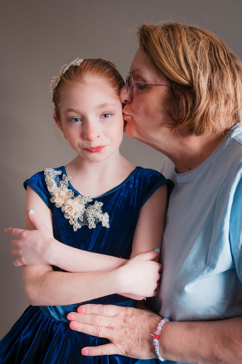 A heartwarming moment between two generations in blue outfits against a gray backdrop, showing care and affection.