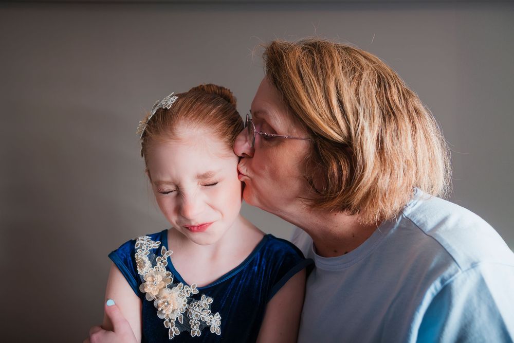 Tender moment shared between parent and child wearing blue dress with floral details against gray background.