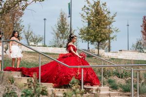 Elegant red ball gown flowing across stone steps in an outdoor setting.