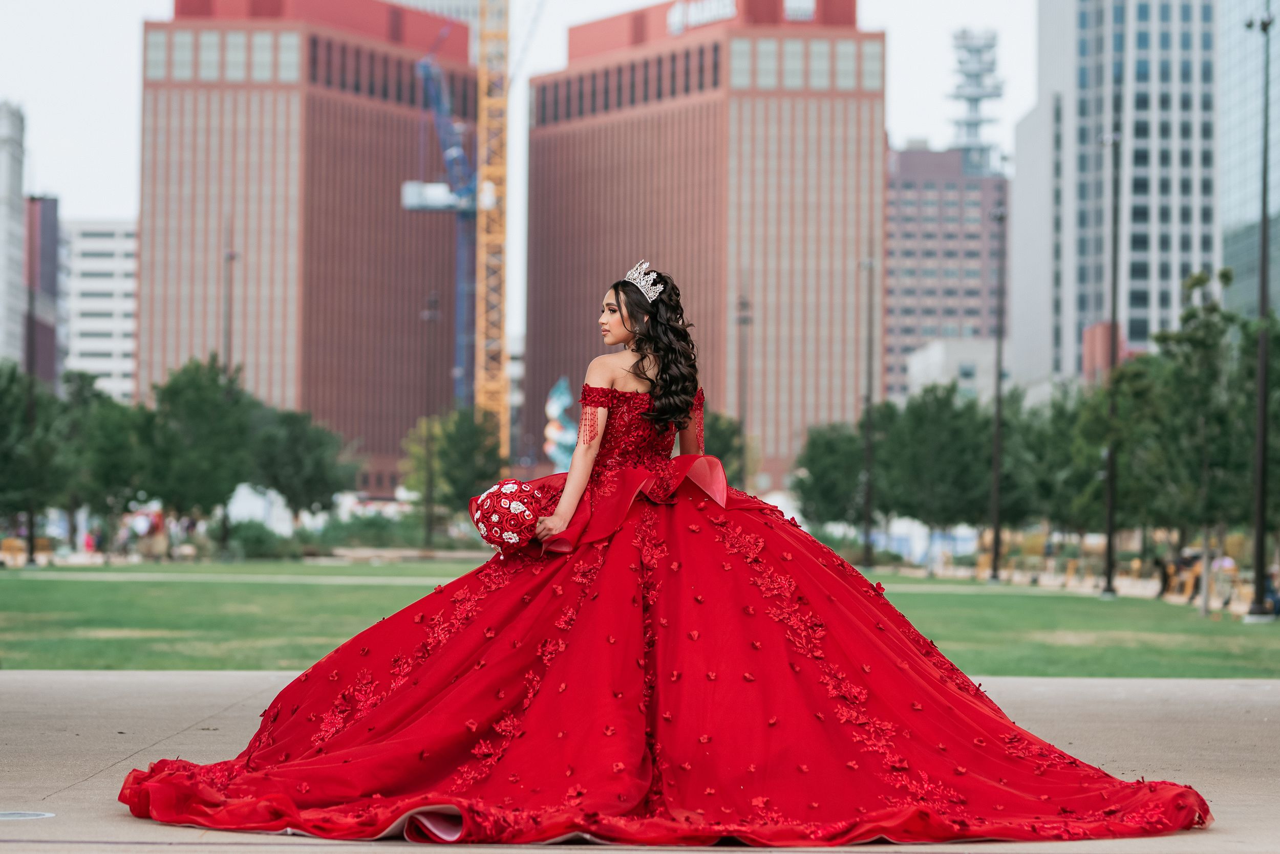 Vibrant red quinceañera dress photographed against an urban cityscape backdrop.