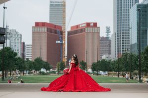 A stunning red quinceañera dress photographed against a city skyline backdrop.