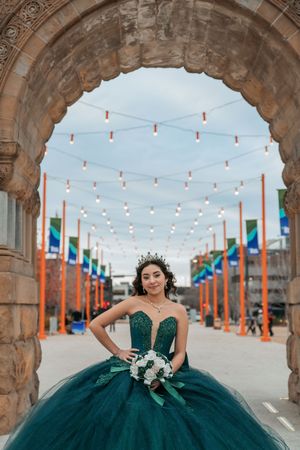 Stunning emerald ballgown photographed under historic stone arches with festive string lighting.