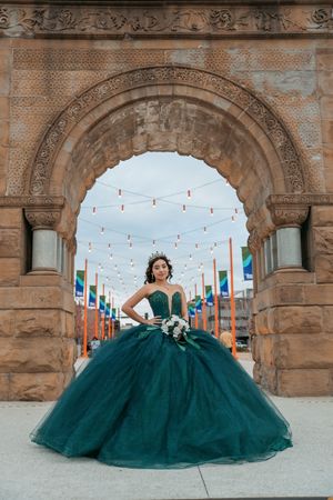 Dramatic emerald green formal dress captured under ornate stone archways with hanging lights.