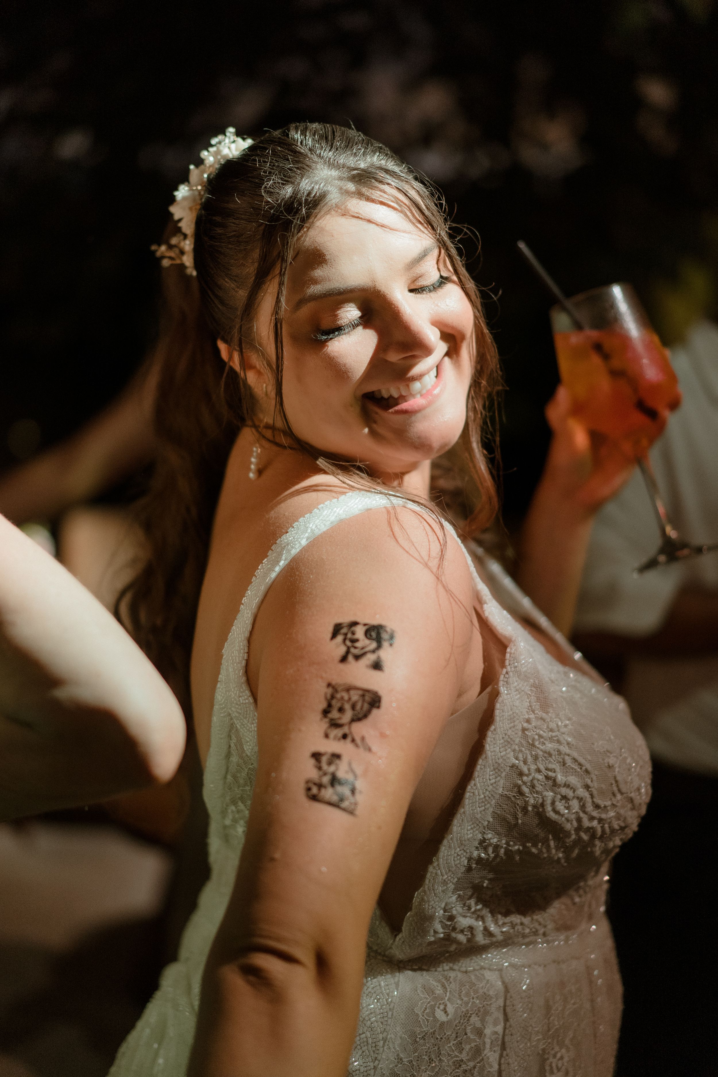 Person in white lace dress showing off temporary tattoos on their arm during a celebration.