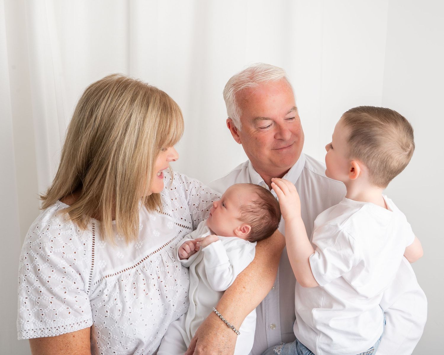 Multi-generational family poses together in a relaxed indoor setting against a white backdrop.
