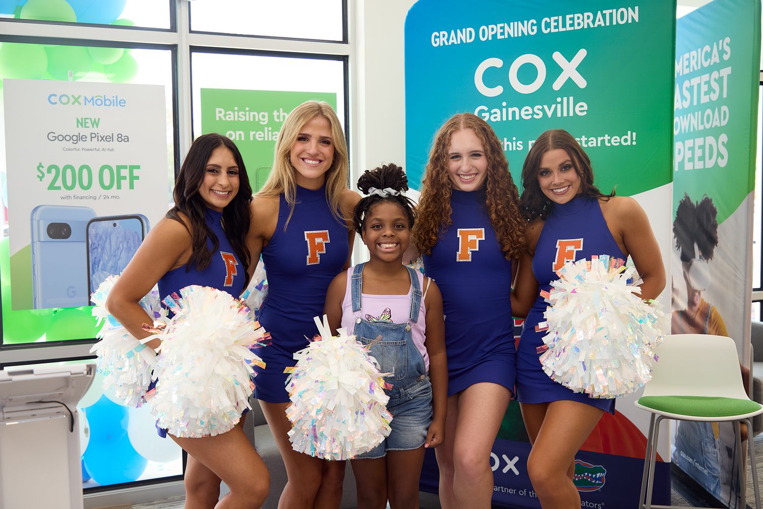 A group poses together under a festive balloon arch with orange, blue and silver balloons against a blue background.