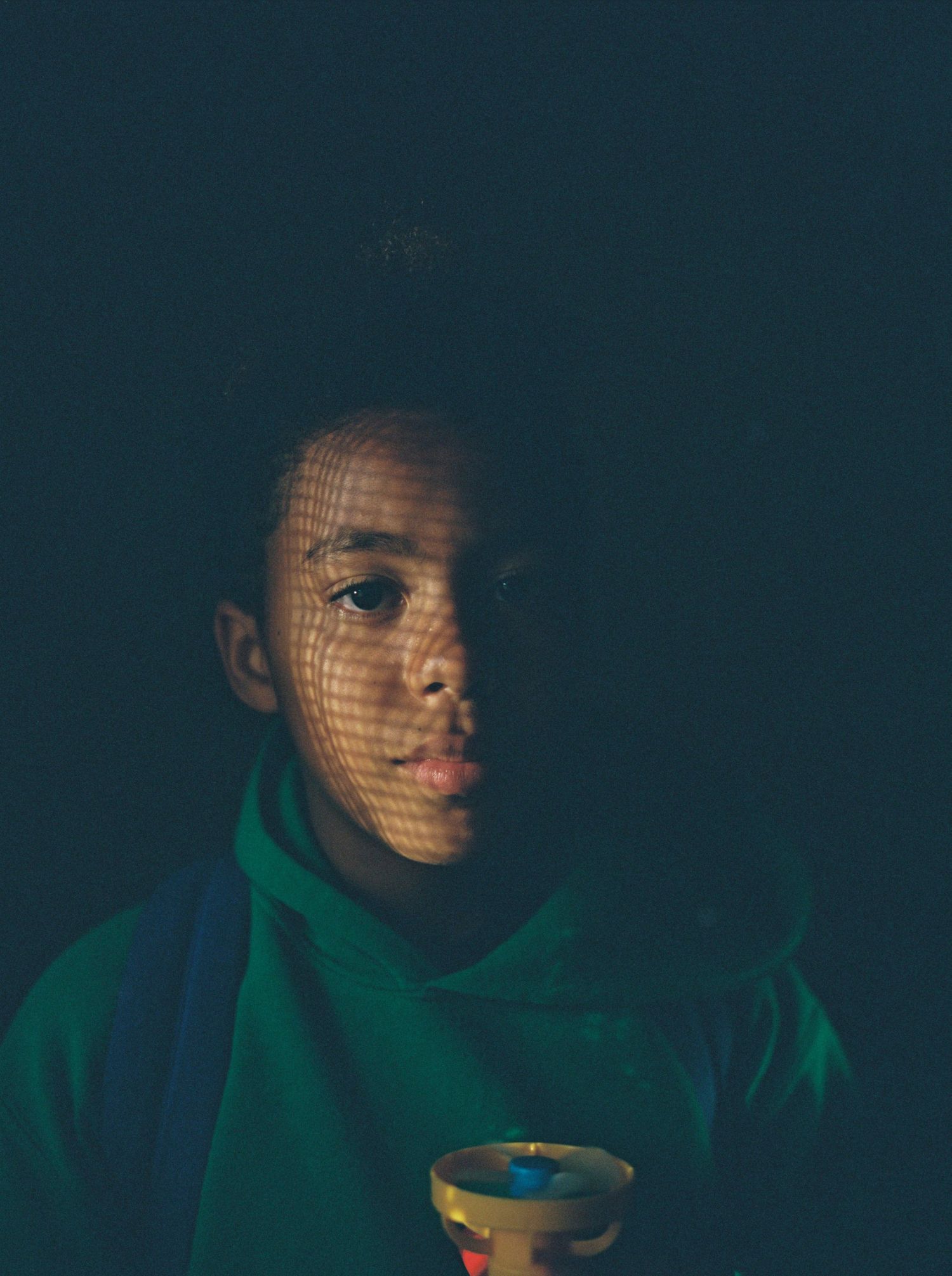 Artistic portrait with green hoodie and dramatic lighting creating a mesh shadow pattern.