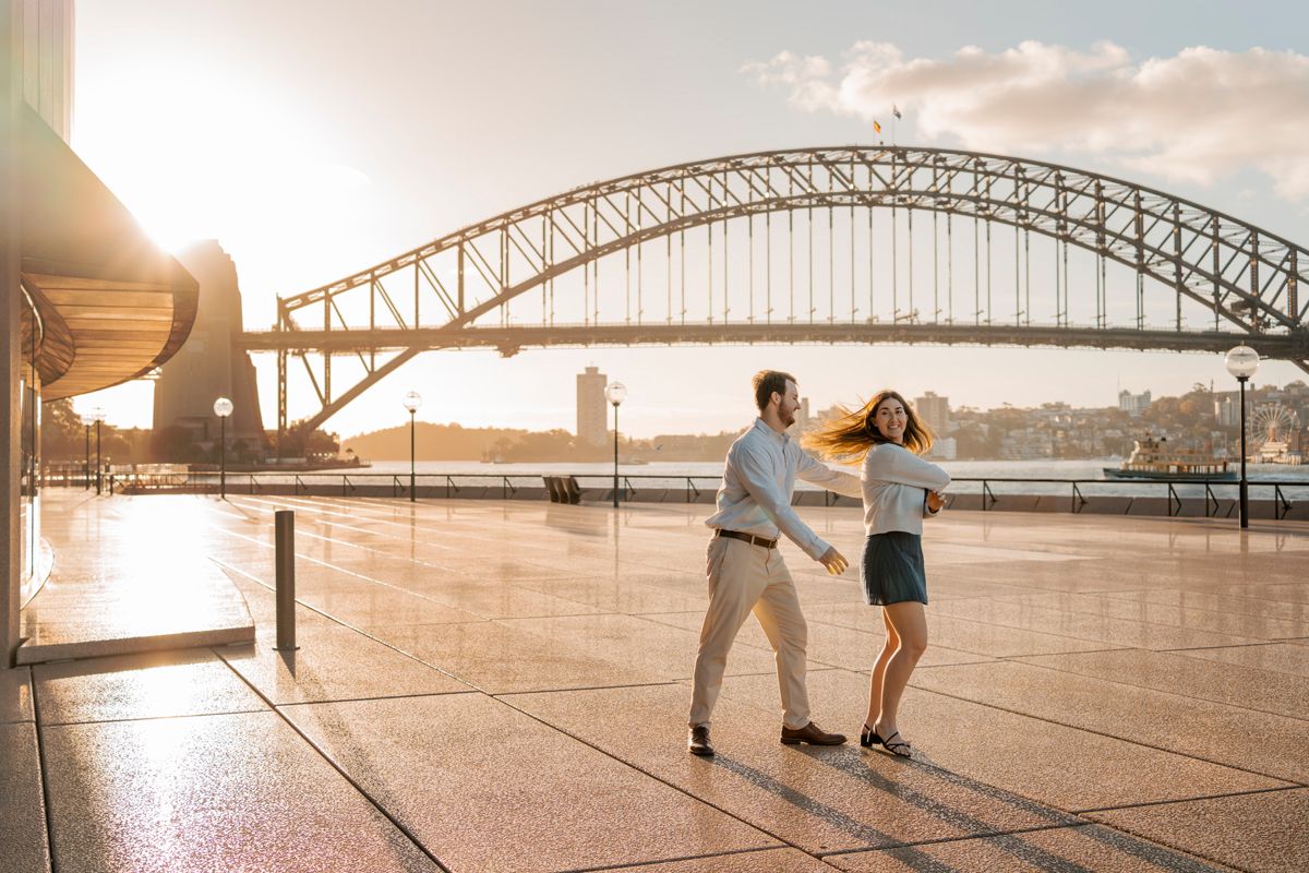 dancing couple during a proposal photoshoot in Sydney with the harbour bridge in the background while the sun is setting with an orange glow