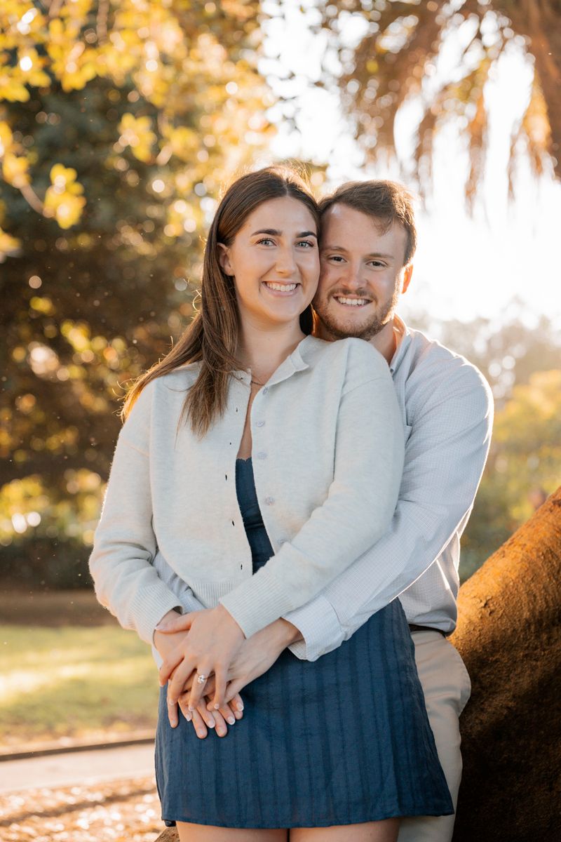 man is cuddling up her newly proposed girlfriend near a fig tree in Sydney during a proposal photoshoot