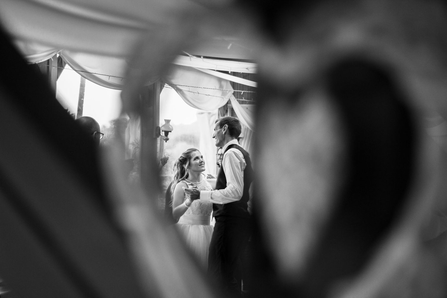A romantic black and white wedding moment framed through a heart shape in the foreground.