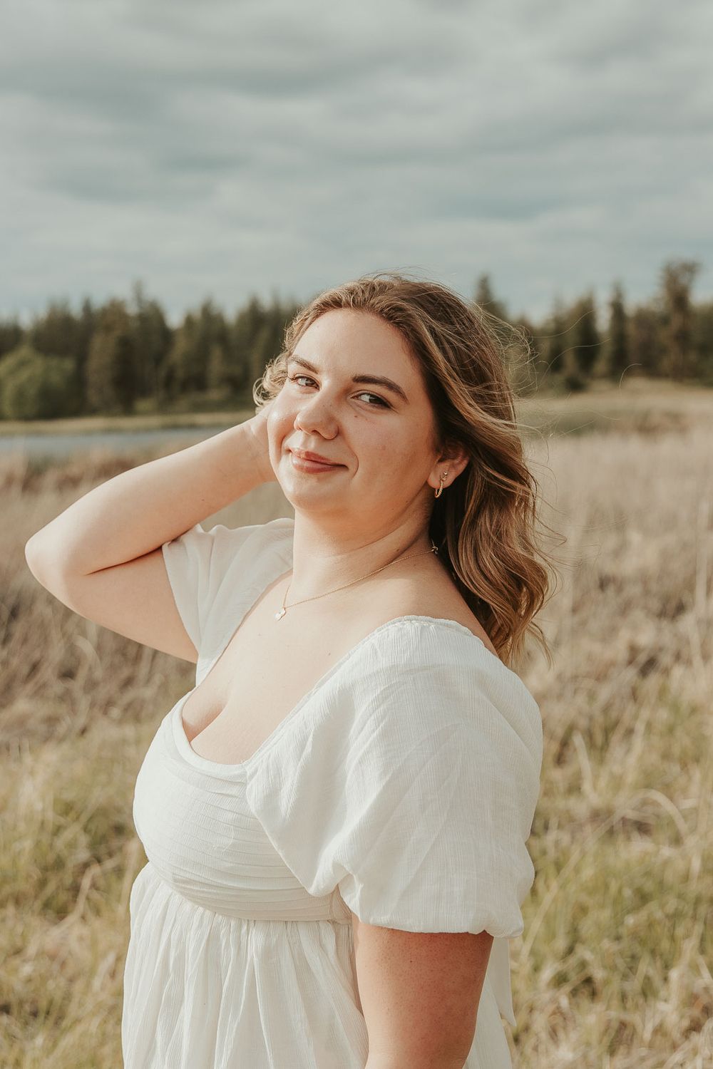 Boho senior session outfit ideas for spring and summer photography. Senior girl smiling in meadow near lake with soft golden lighting