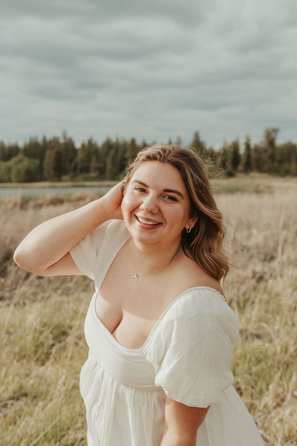 Boho senior session outfit ideas for spring and summer photography. Senior girl smiling in meadow near lake with soft golden lighting