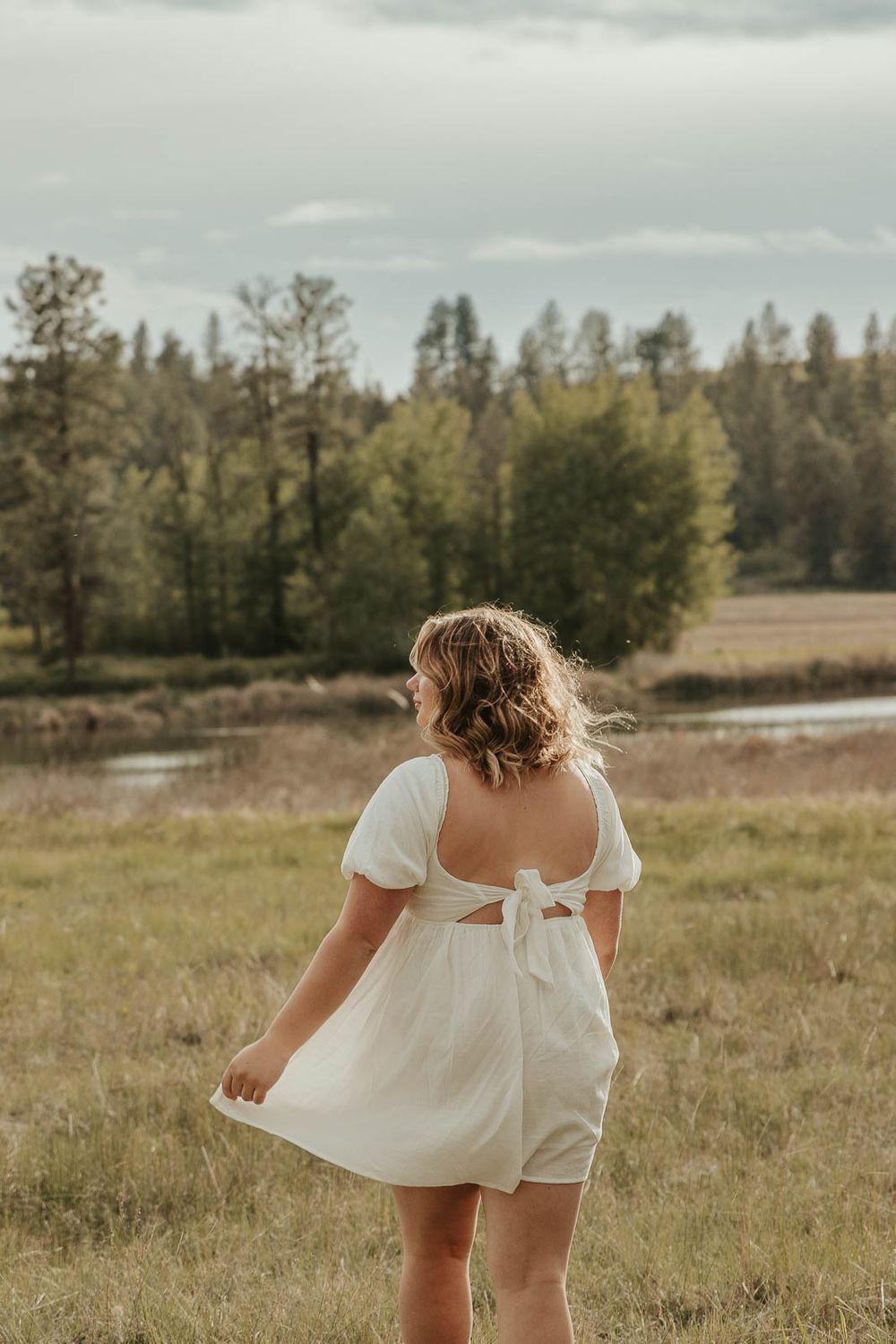 Boho senior session outfit ideas for spring and summer photography. Senior girl smiling in meadow near lake with soft golden lighting