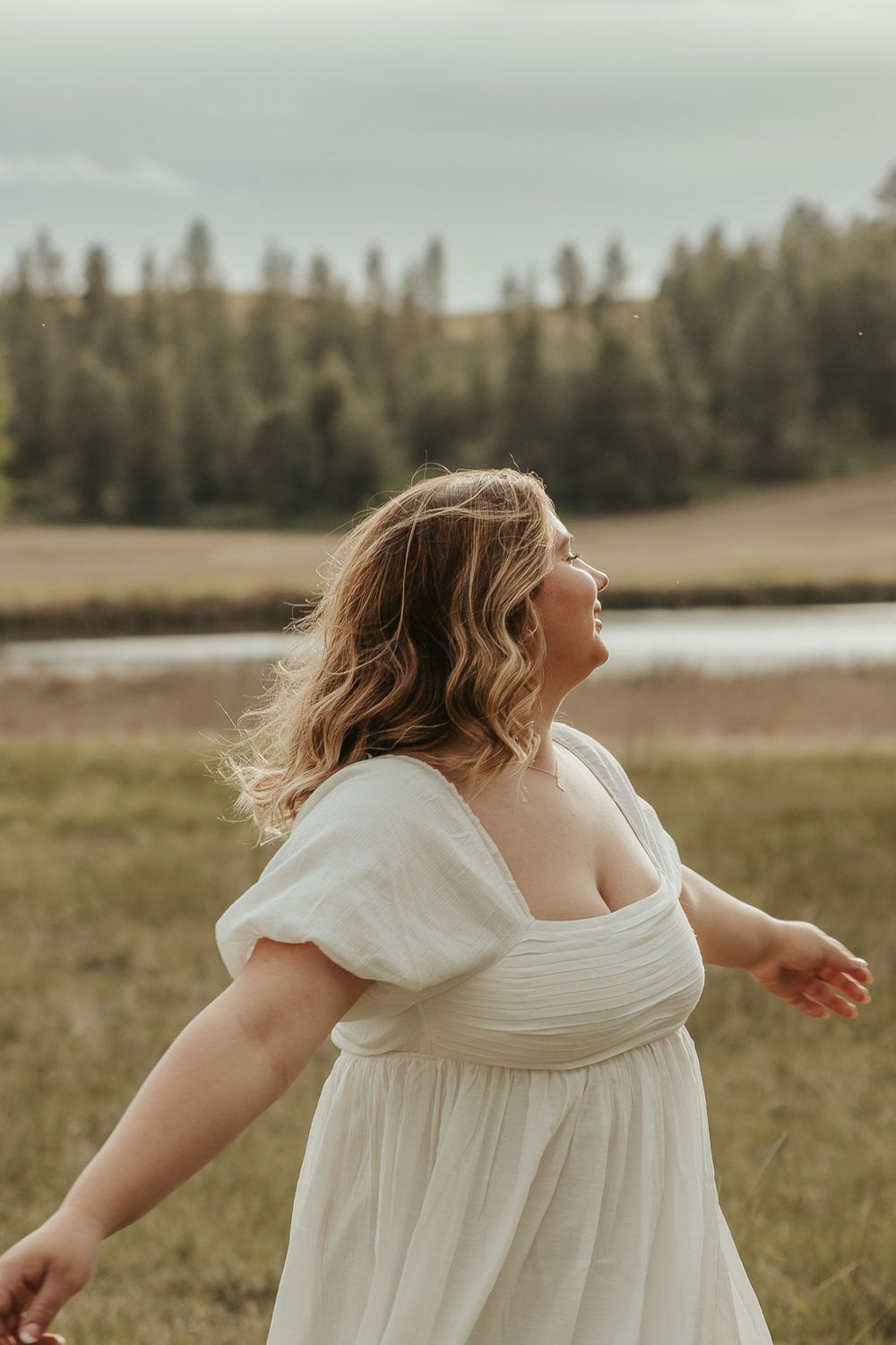 Boho senior session outfit ideas for spring and summer photography. Senior girl smiling in meadow near lake with soft golden lighting