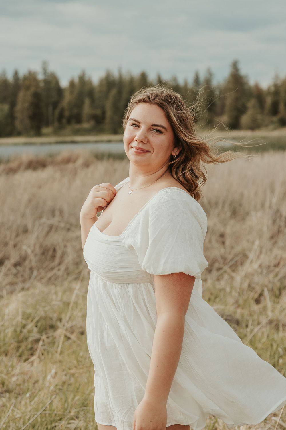 Boho senior session outfit ideas for spring and summer photography. Senior girl smiling in meadow near lake with soft golden lighting