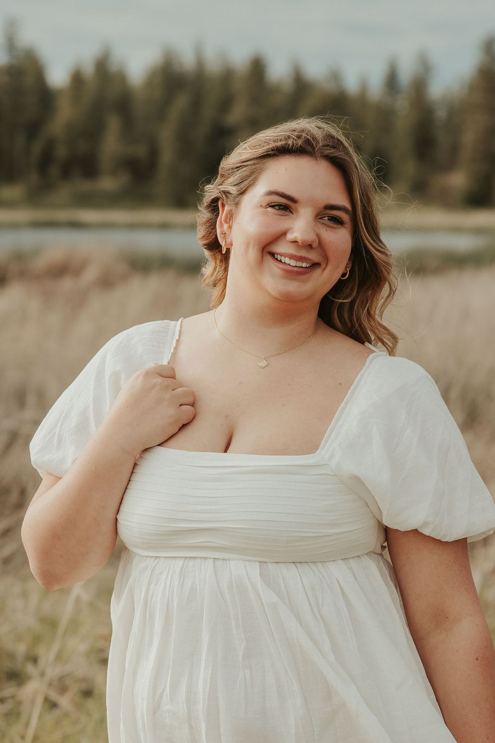 Boho senior session outfit ideas for spring and summer photography. Senior girl smiling in meadow near lake with soft golden lighting