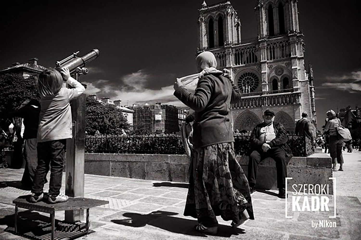 Fotografia uliczna przed katedrą Notre-Dame – dziecko przy lunecie, kobieta w chuście, emeryt – uchwycony przez Anetę Ludwig. Nikon.