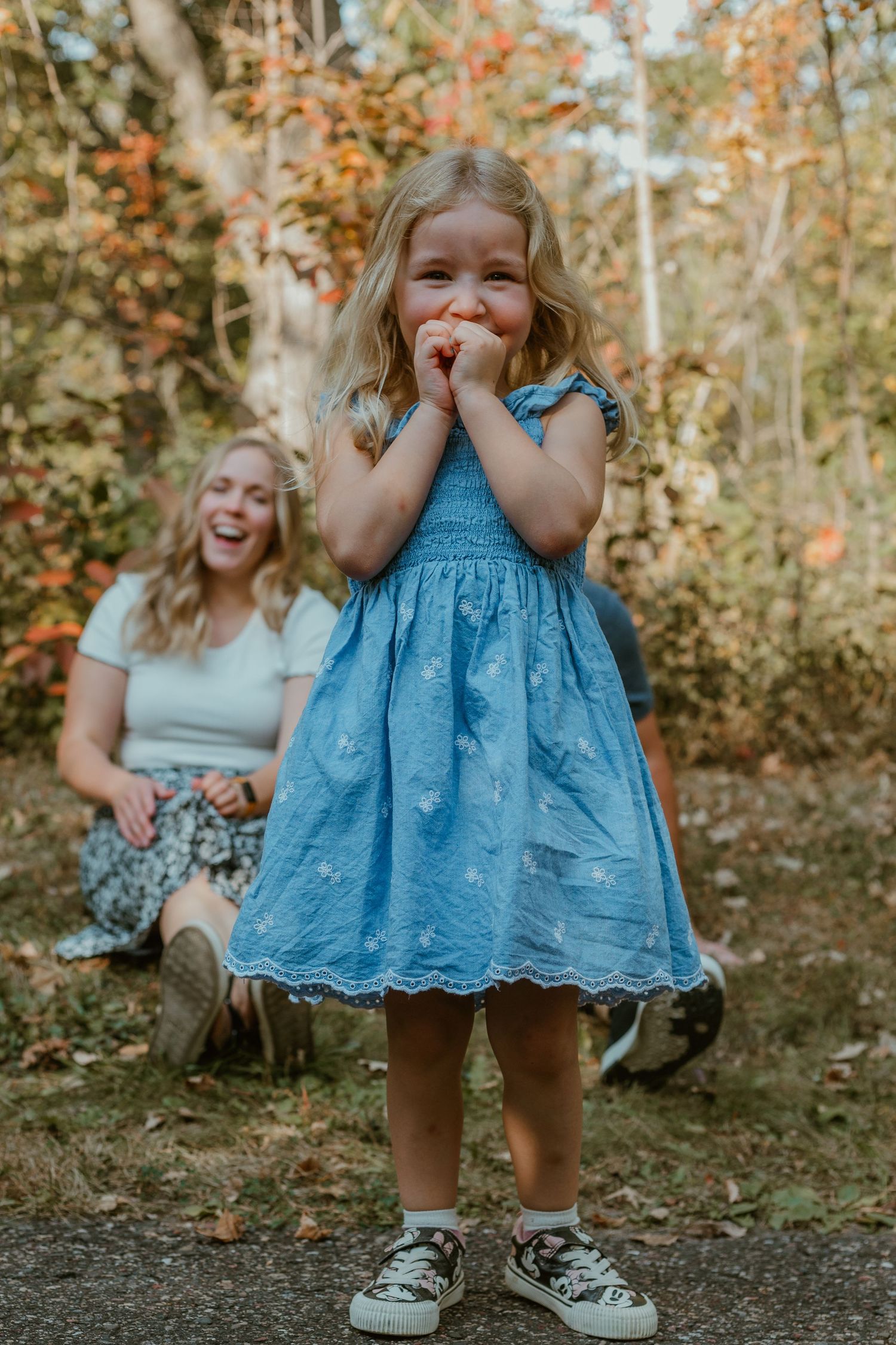 A playful family portrait in autumn with matching blue dresses enjoying a candid moment in the woods.
