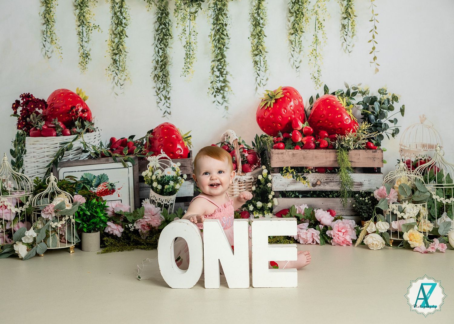 Floral first birthday photoshoot setup with wooden crates, red peonies and cascading greenery against white backdrop.