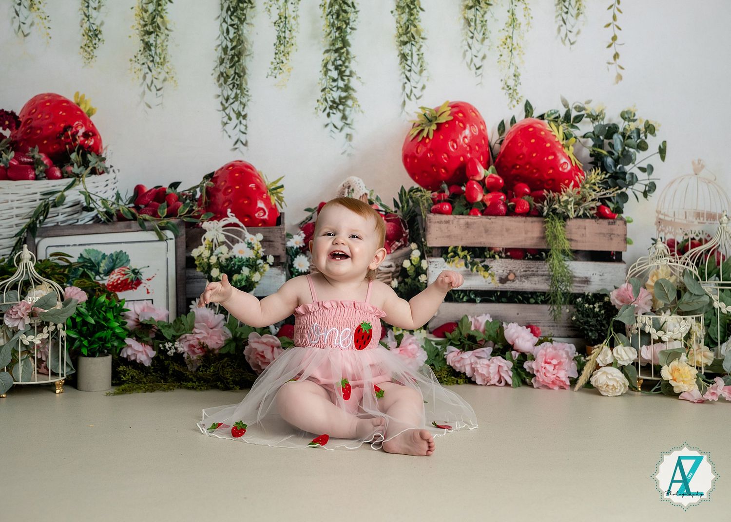A small child sits on a white floor surrounded by decorative red flowers and greenery in a studio setting.