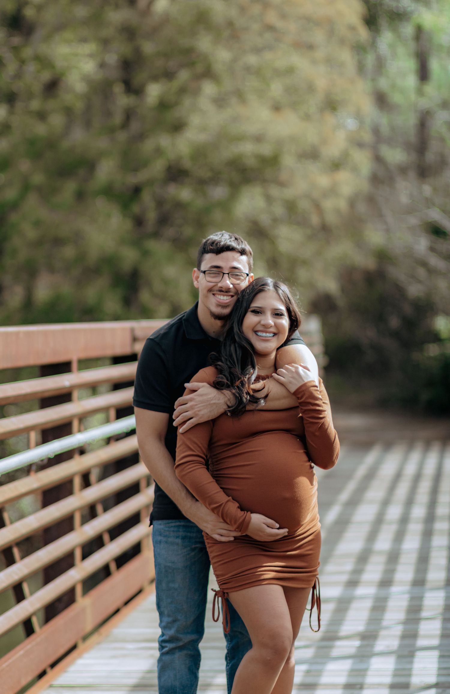 Couple posing on a wooden bridge for a maternity photo shoot outdoors.