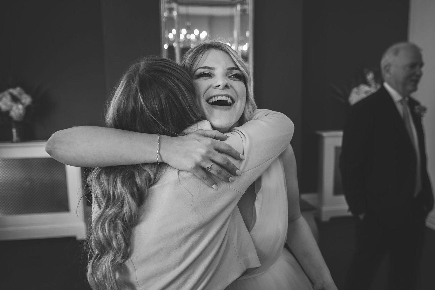 The bride shares a joyful embrace with a guest in a black and white candid moment after the ceremony.