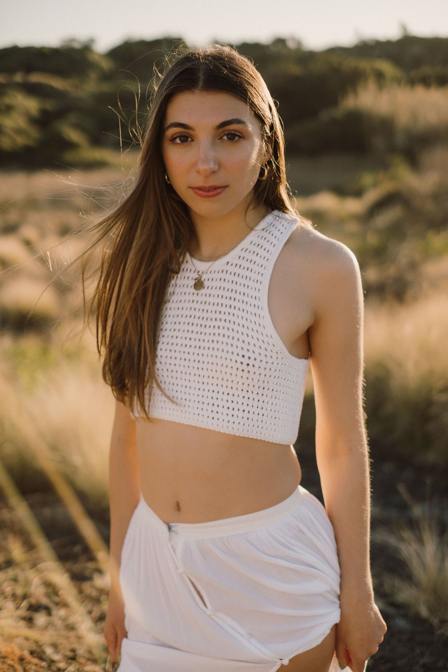 Woman in white lace lying gracefully on sandy beach during golden hour.