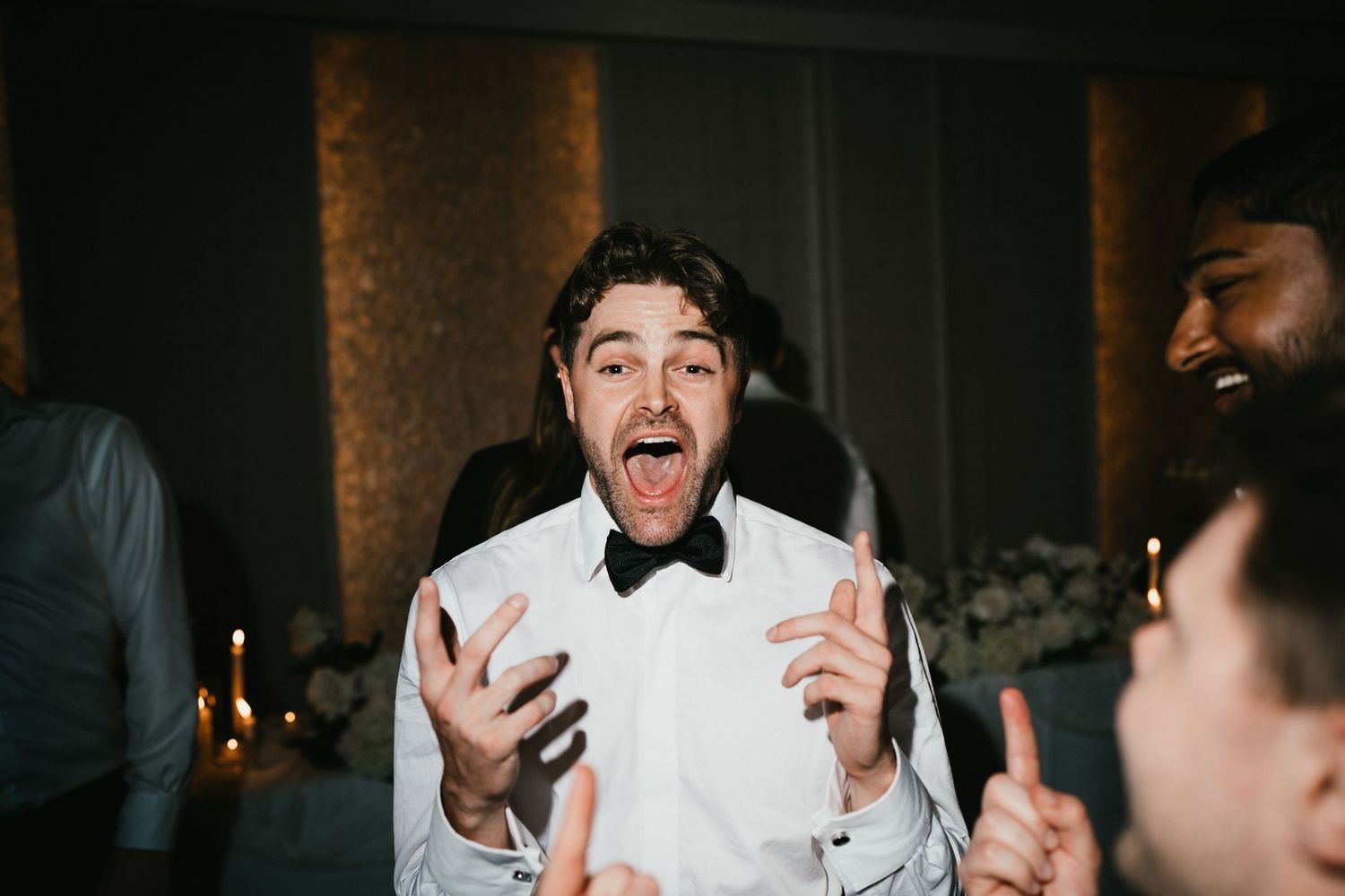 A person in a bowtie and white shirt reacts with excitement at a formal event.