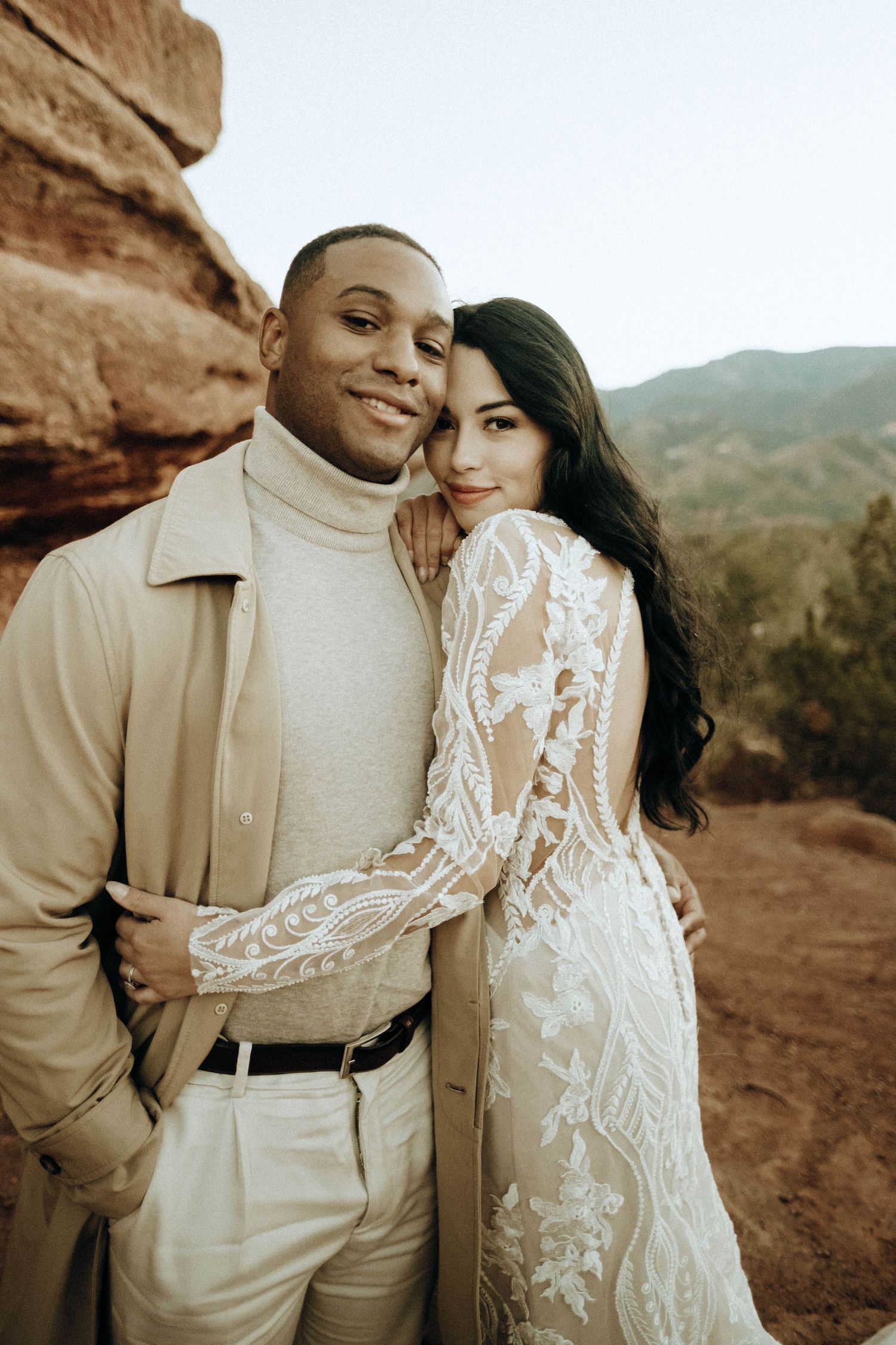 Interracial wedding couple poses in red rock canyon, bride in lace gown embracing groom.