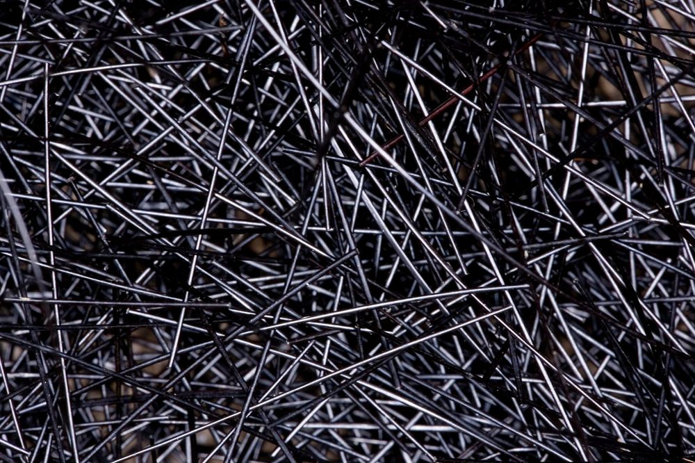 Abstract pattern of scattered black metal nails creating chaotic texture.