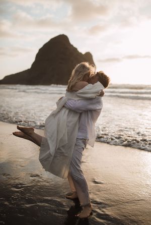 Romantic beach photoshoot with couple in white clothing dancing in the surf at sunset.