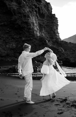 Black and white beach photoshoot with flowing white outfits against dramatic coastal cliffs.
