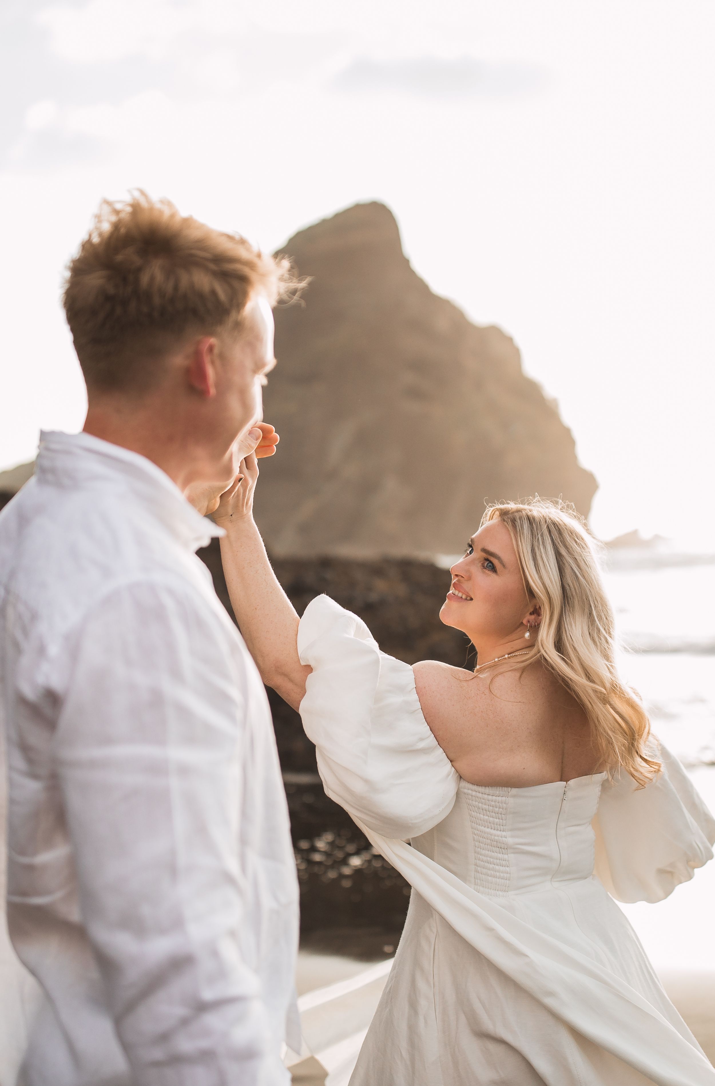 Sunset beach photoshoot with flowing white clothing and dramatic coastal rock formations.