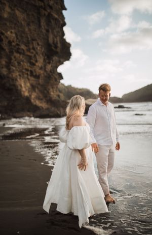 Couple walking along a dramatic black sand beach with towering coastal cliffs.