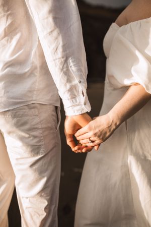 Close-up shot of two people in white clothing holding hands.