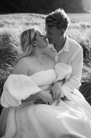 Black and white portrait of a couple in white clothing sitting close together in beach grass.