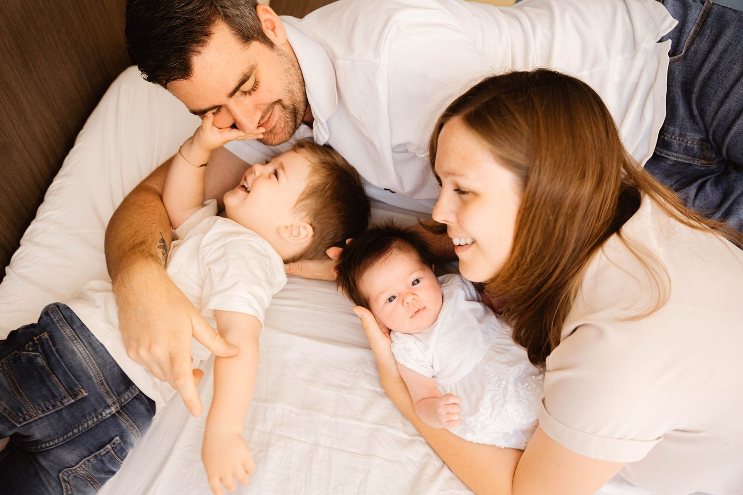 Family cuddle moment on bed in white clothing.