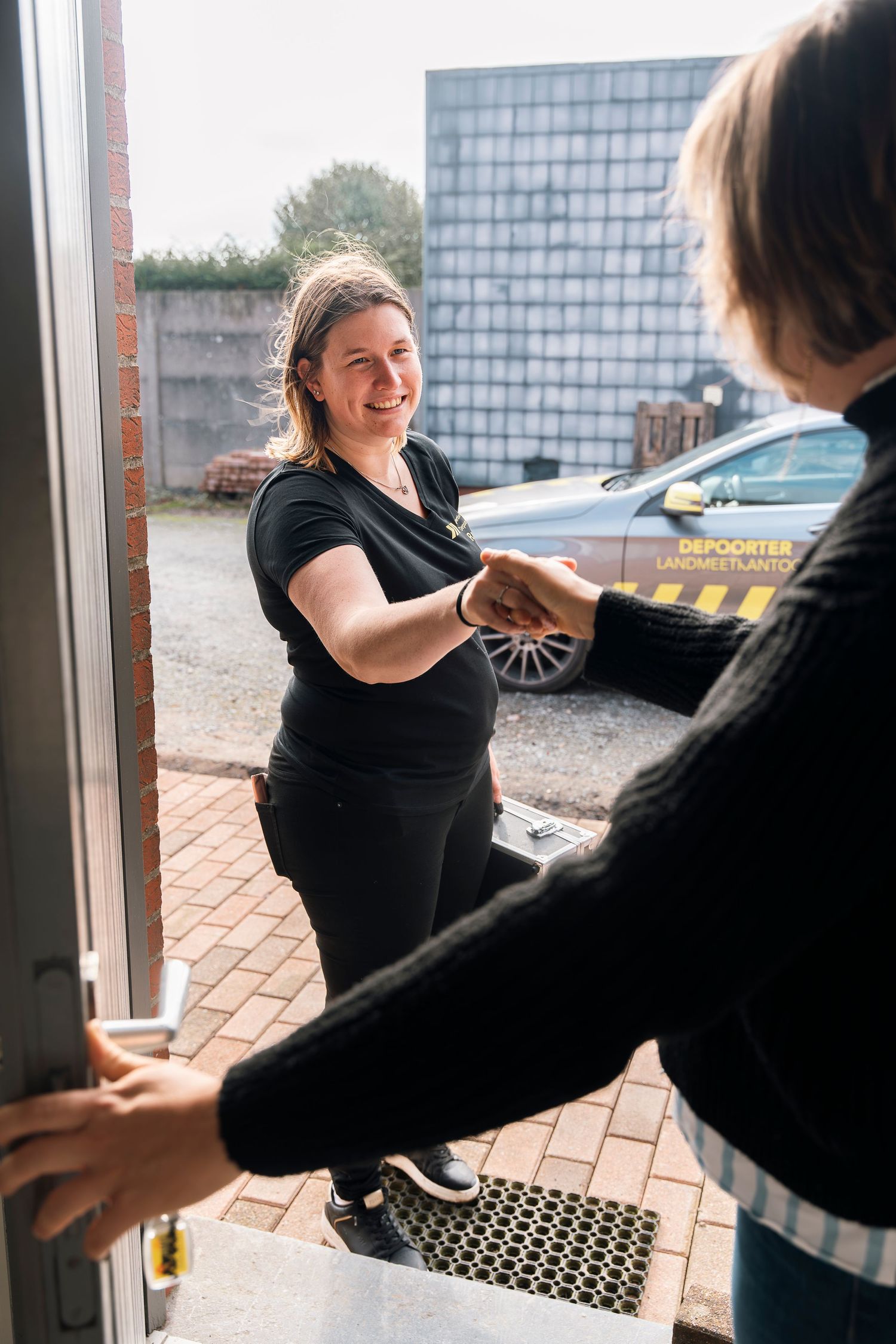 Professional in black uniform warmly greeting someone at entrance with a friendly handshake.