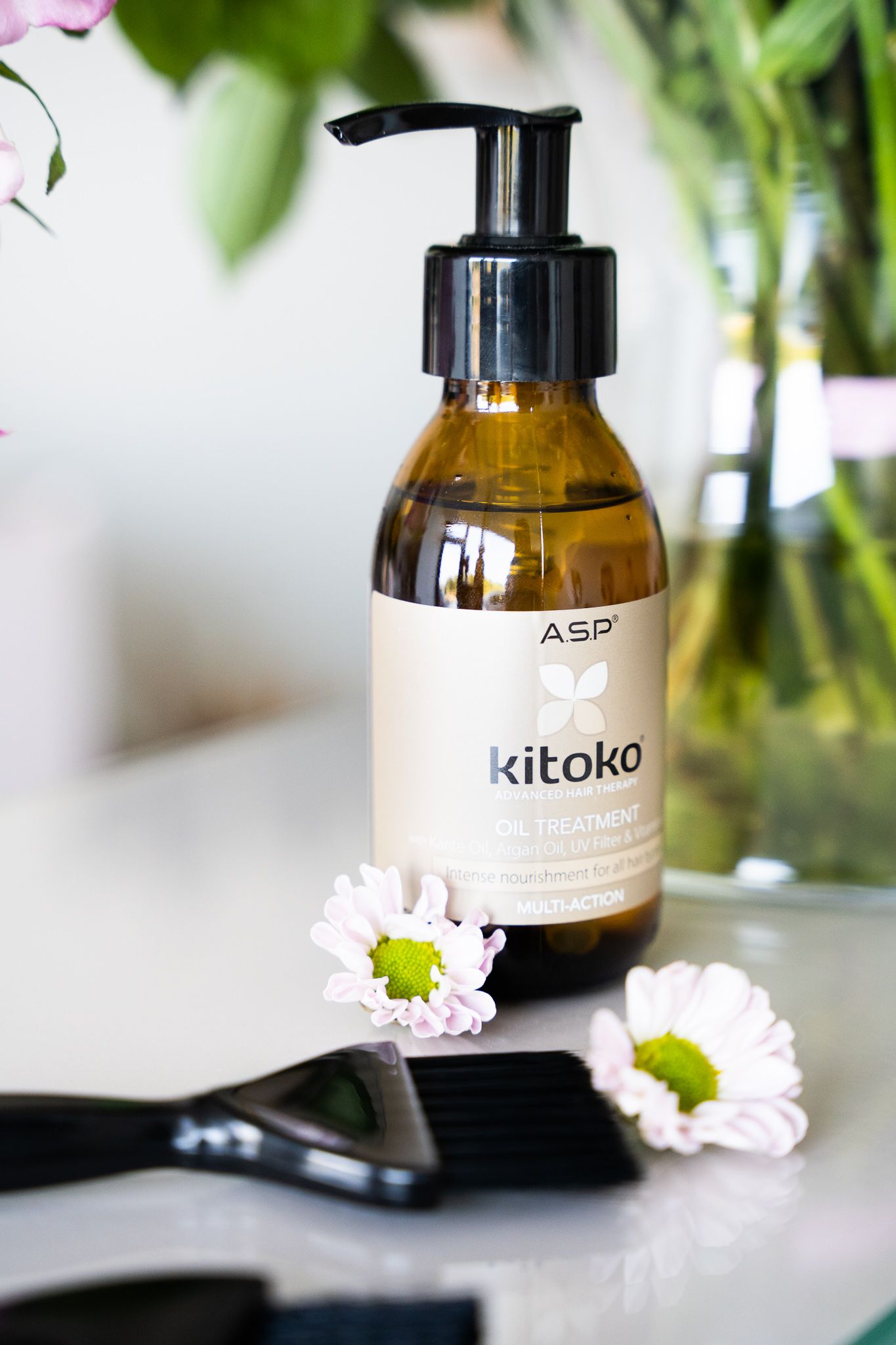 Kitoko hair treatment bottle with daisies and styling tools against blurred background.