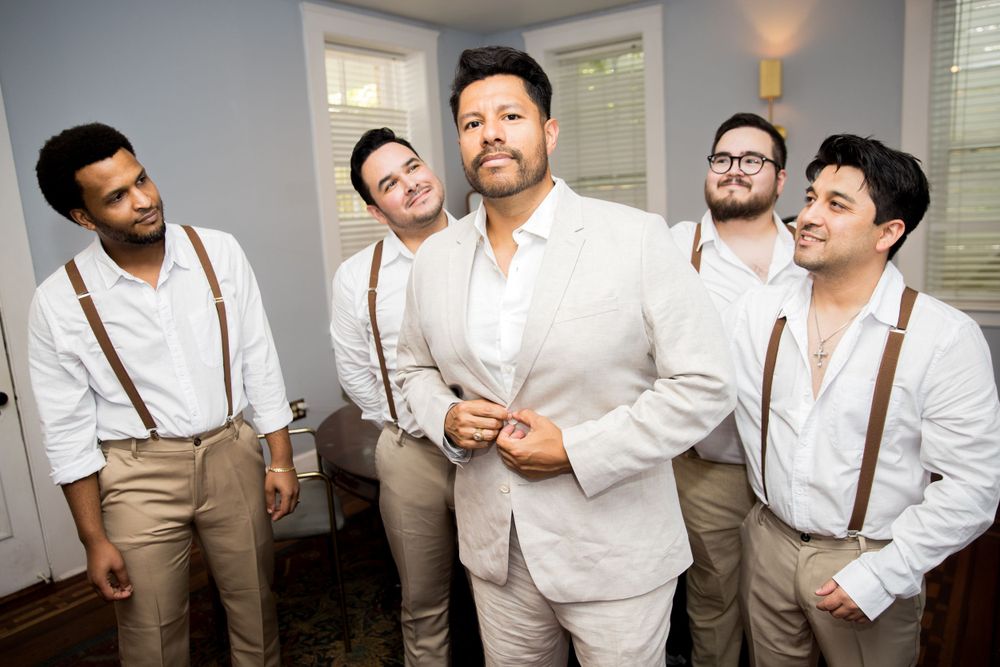 Wedding party in coordinated white shirts and suspenders posing together.