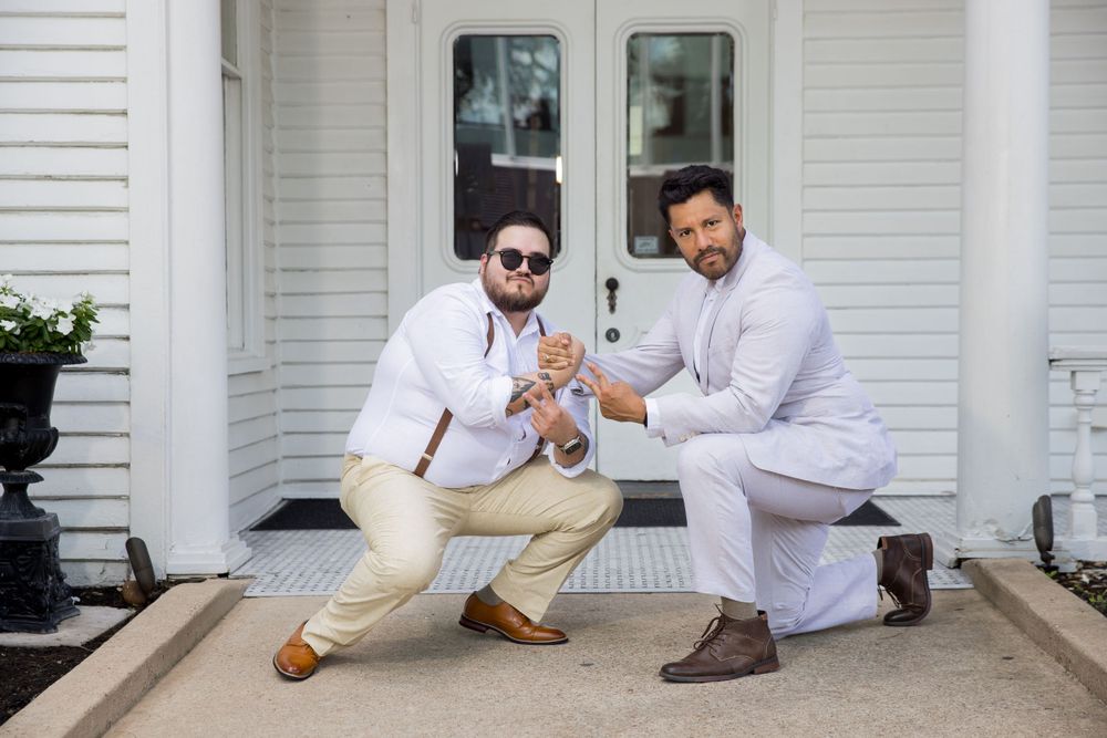 Two people in light colored formal wear strike fun poses on white porch.
