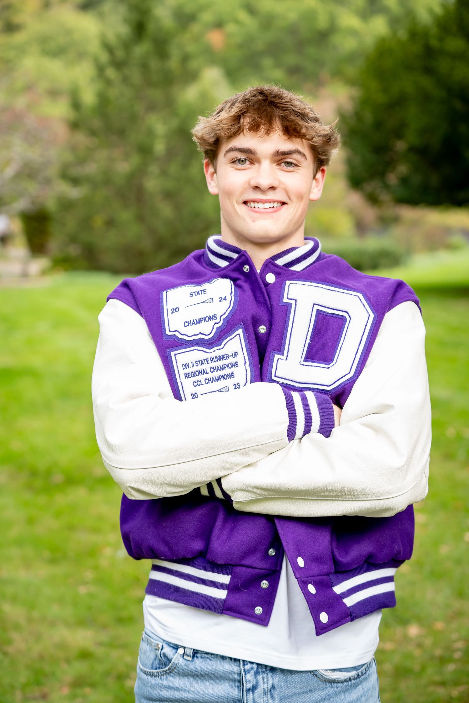 Varsity letterman jacket in purple and white shown in multiple closeup views outdoors against green background.