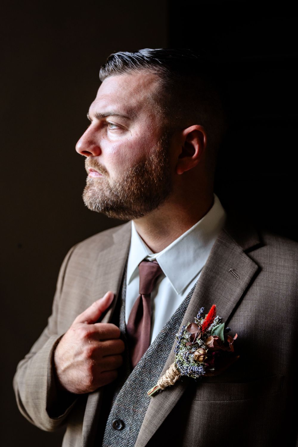 Close-up detail of a grey suit jacket with boutonniere in dramatic lighting.