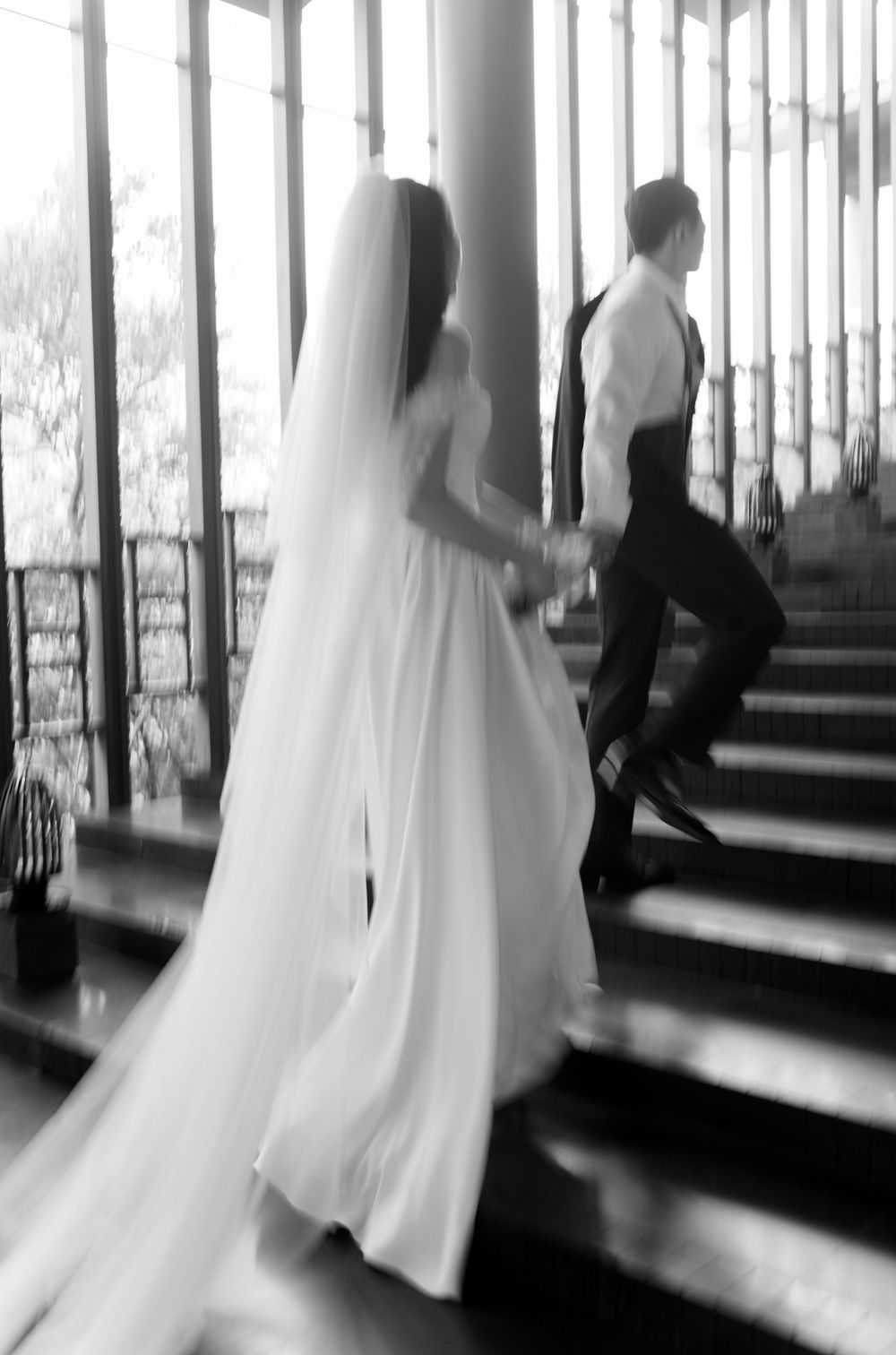Ethereal black and white photo of flowing white wedding dresses moving through a light-filled hallway.