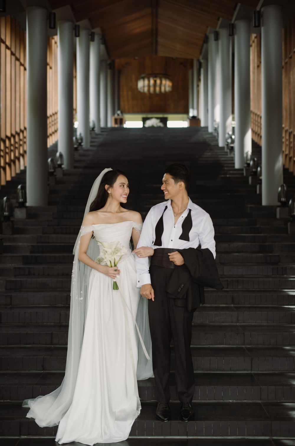 Wedding couple on grand staircase with elegant columns in architectural setting.