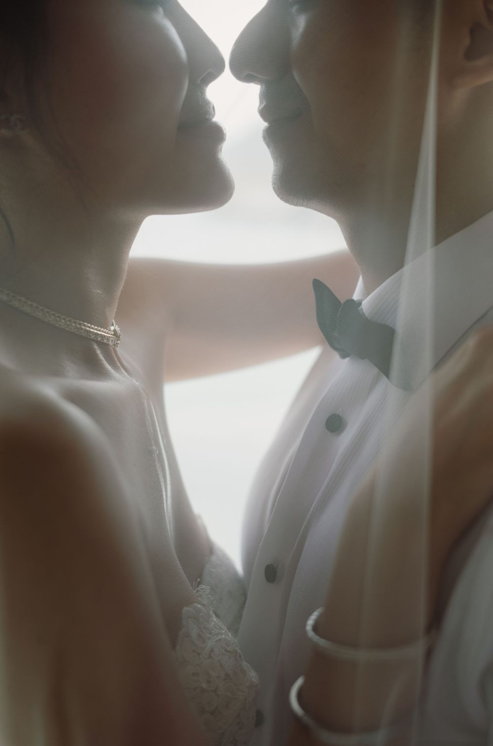 Silhouetted figures in wedding attire share an intimate moment backlit by soft natural light.