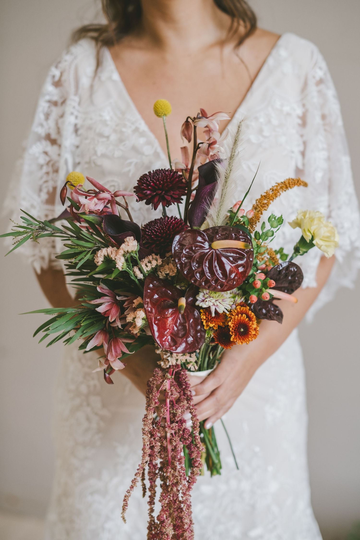 Close-up shots of a wedding bouquet with burgundy dahlias, pink flowers and textural greenery held against a lace dress.