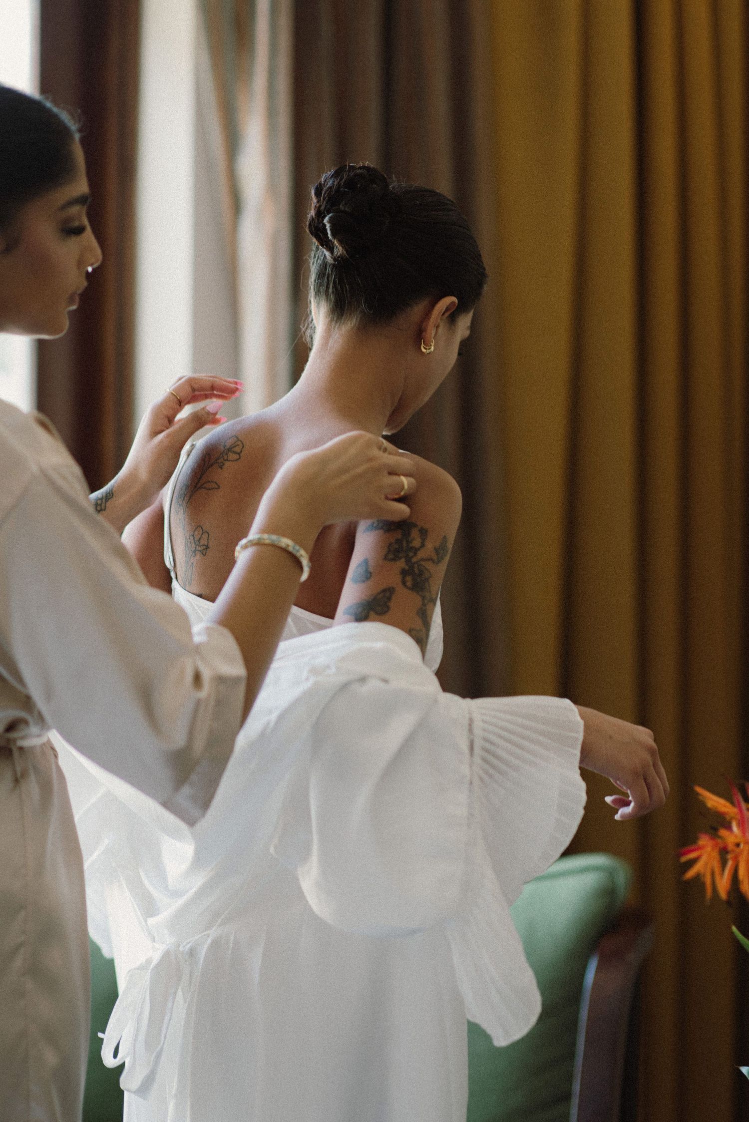 Bride getting ready in an ethereal white robe with ruffled sleeves against golden curtains.