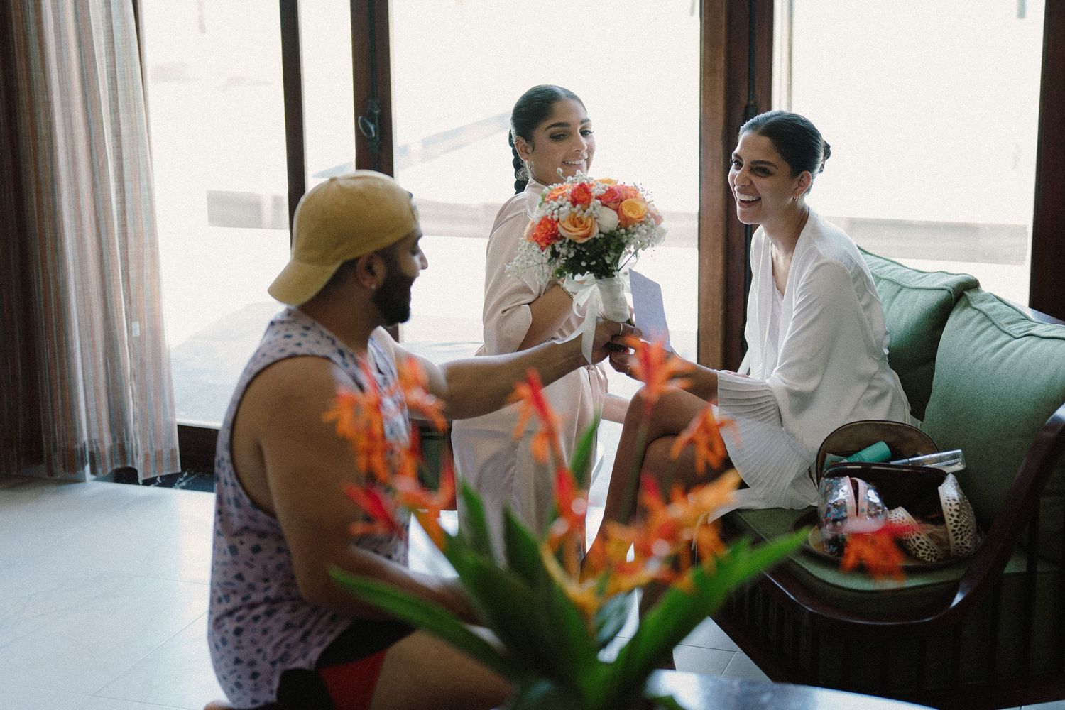 Group gathers near window with orange flowers and white curtains in background.